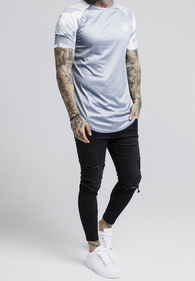 T-shirt de sport gris clair avec des manches courtes à motif camouflage, associé à un jean skinny noir déchiré et des baskets blanches.