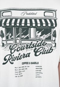 Façade d'un café avec un auvent rayé, panneau « Interdit », texte « Courtside Riviera Club » et menu listant diverses options de café et de bagels.