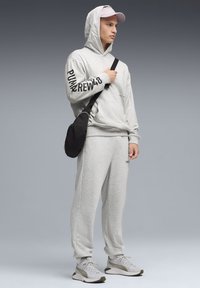 Sweat-shirt gris à capuche et manches longues, arborant le texte "PUMA REW48". Associé à un pantalon de survêtement gris assorti et un sac bandoulière noir.