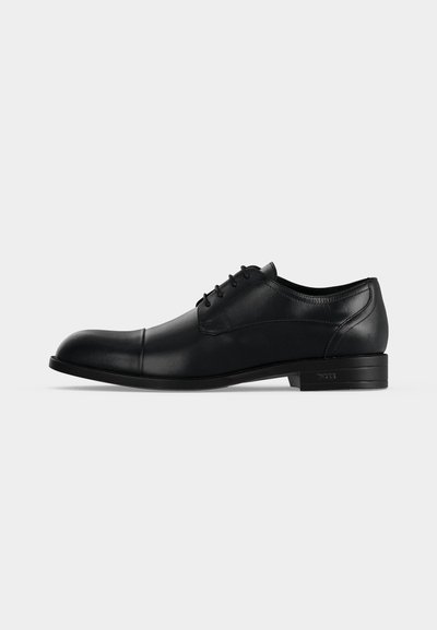 Chaussure habillée pour homme en cuir noir avec lacets, bout droit et petit talon, vue de profil sur un fond gris clair uni.