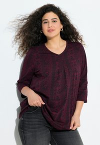 Haut bordeaux à motifs avec des manches trois-quarts, un décolleté en V et une coupe décontractée, associé à un jean noir pour un look décontracté.