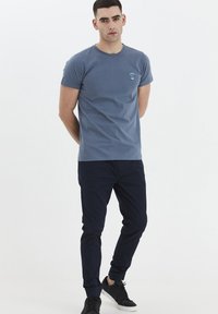 Blue cotton t-shirt with a crew neckline, featuring a small graphic design, paired with navy elasticated pants and black sneakers.