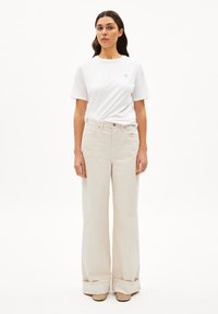 Witte korte mouwen t-shirt met een klein geborduurd logo, gecombineerd met beige rechte pantalons met opgerolde manchetten en een subtiele textuur.