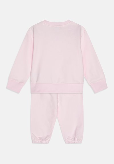 Rozā džemperis un bikses komplekts, izgatavots no mīkstas kokvilnas. Džemperim ir apaļš kakls un ribota piedurknes; biksēm ir elastīgas potītes un aizmugures kabata.