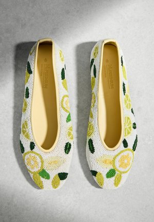 Pair of cream-colored ballet flats with yellow and green beaded lemon slice and leaf patterns on a gray surface.