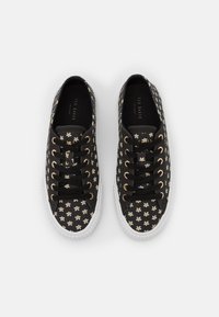 Black canvas sneakers with white rubber soles, featuring floral patterns in white and yellow, and gold-toned eyelets.