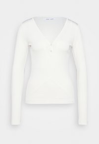 Maglia bianca a maniche lunghe con scollatura a V e dettagli con bottoni, esposta su uno sfondo bianco semplice.