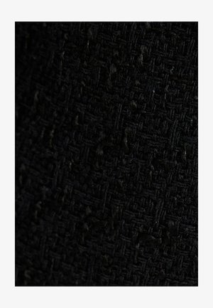 Tessuto nero texturizzato con un motivo intrecciato, che mostra un mix di elementi di superficie liscia e soffici, creando profondità e interesse visivo.