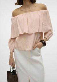 Top rosa off-the-shoulder con volantini sovrapposti, maniche lunghe a sbuffo e una texture liscia, abbinato a una gonna bianca e una borsa marrone.