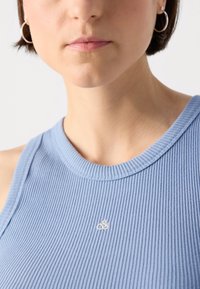 Hellblaues, geripptes Tanktop mit rundem Ausschnitt und kleinem, weißem gesticktem Logo auf der Brust. Einfaches Design ohne Muster.