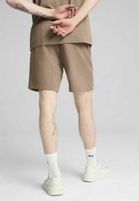 Pantalones cortos de algodón marrón con cintura elástica, combinados con calcetines blancos y zapatillas crema. Se ve un tatuaje en la pantorrilla.