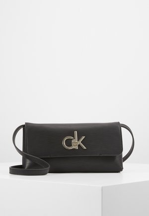 Black textured leather crossbody bag with slim strap and metallic "CK" logo clasp, displayed on a white pedestal against a plain background.