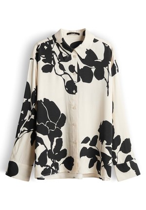 Blusa crema con maniche lunghe e bottoni, con grande stampa floreale nera e colletto a punta, mostrata distesa su sfondo bianco.