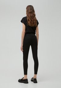 Black fitted t-shirt with rolled sleeves paired with black skinny jeans. The model wears black loafers with a chunky sole.