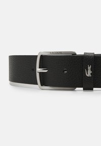 Black leather belt featuring a textured surface, silver metal buckle with engraved brand name, and a small silver crocodile logo accent.