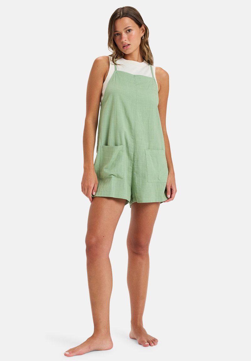 Vestido overall de algodón verde claro con tirantes ajustables, bolsillos frontales y un corte relajado, que presenta una tela texturizada para un detalle adicional.