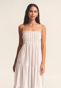 Vestido blanco con rayas verticales rojas y azules, cuerpo fruncido, tirantes finos ajustables y bajo con volantes en capas. Material de algodón con textura ligera.