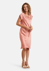 Kleid mit Kragen, knielang aus weichem pinken Stoff, mit kurzen Ärmeln und einem Bindeband in der Taille. Es hat einen lässigen Schnitt und eine glatte Textur.