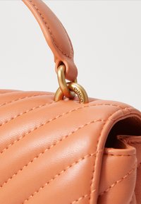 Persikofärgad läderhandväska med kviltad design, guldhardware och ett runt handtag. Har synlig söm och en märkesring i metall.