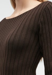 Ruda, ilgarankovė marškinėlių viršutinė dalis su raukšlėtu audiniu, platų iškirptę turinti, su vertikaliomis juostelėmis, suteikiančiomis papildomą matmenį.