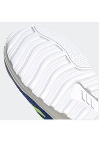 Bílá gumová podrážka s texturovanými drážkami, modrý svršek a limetkově zelené akcenty na boku. Design je sportovní se zaměřením na přilnavost.