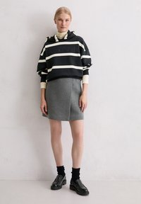 Black and white striped cropped hoodie with logo, gray wool blend skirt, black platform shoes, and black ribbed socks.