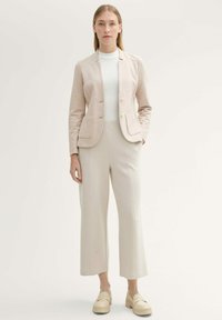 Blazer ajusté beige clair à deux boutons et poches avant, associé à un pantalon large crème et des mocassins à plateforme. Tissu texturé.