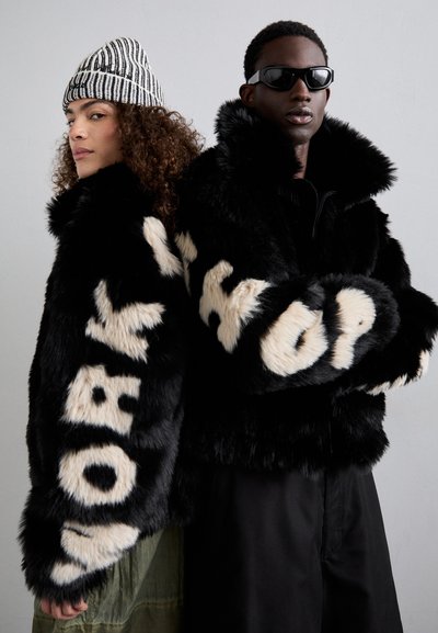 Chaquetas de piel sintética negra con letras crema que dicen "WORK" y "HOP" en las mangas. Ambos modelos llevan accesorios de patrones contrastantes y gafas de sol elegantes.