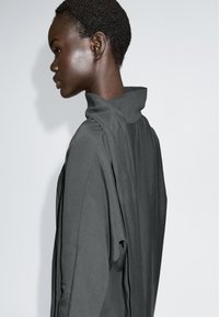 Szara, długosleeve odzież z wysokim kołnierzem i drapowaniem z tyłu. Gładka tekstura i nowoczesny krój. Prosty design bez wzorów i akcentów.