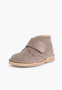 Stivaletto in suede marrone con velcro, punta tonda e suola piatta beige. Presenta una semplice cucitura lungo il bordo della suola.
