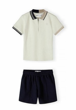 Kremowa koszulka polo z krótkim rękawem z kołnierzykiem i mankietami w czarno-beżowe paski, zestawiona z czarnymi szortami z elastycznym paskiem w talii.