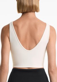 Kvinna med kort blont hår som bär en texturerad vit ärmlös crop top med djup V-mage och svarta högmidjade byxor.