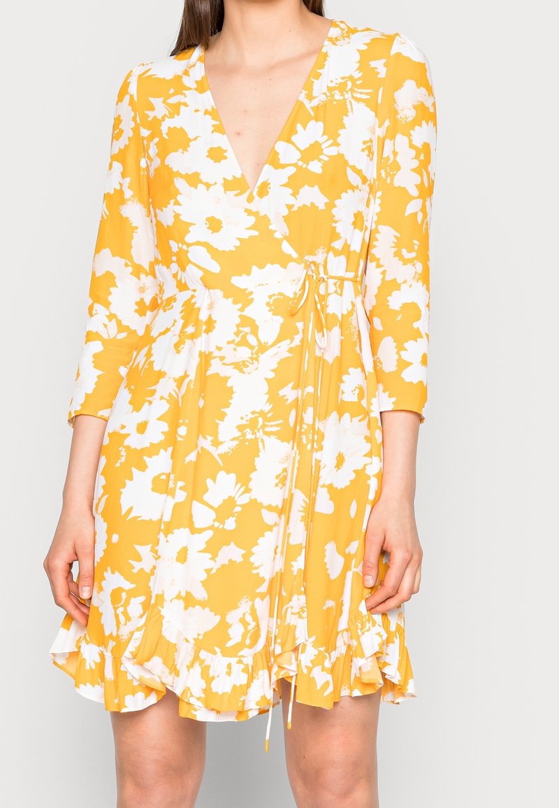 Robe florale jaune avec un décolleté en V, des manches trois-quarts, un ourlet à volants et une taille élastique. Fabriquée en tissu léger avec une finition satinée.