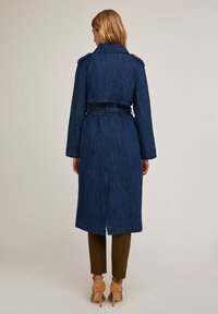 Jeansowy trench w ciemnoniebieskim kolorze, z paskiem w talii, pagonami na ramionach oraz średniej długości fasonem z otworem wentylacyjnym z tyłu.