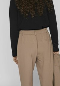 Beige skræddersyede bukser med en glat overflade, elastisk talje og to baglommer. Bæres med en sort langærmet top.
