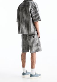 Chemise à manches courtes rayée grise et short assorti, en tissu texturé. Finition avec un logo discret sur la poche arrière.