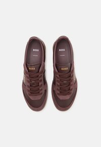 Bordeauxfarbene Sneakers aus Wildleder und Leder, mit runden Zehen und flachen Schnürsenkeln. Verfügt über ein goldenes Logo und klassische Designelemente. Hergestellt in Europa.