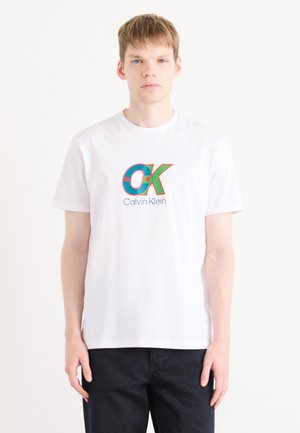 White cotton t-shirt featuring a large, colorful "OK" logo and "Calvin Klein" text. Simple crew neck and short sleeves.