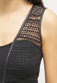 Top sin mangas negro con intrincados detalles de encaje en el hombro y patrones geométricos, textura suave y forma ajustada.