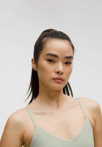 Top verde deschis fără mâneci, cu bretele subțiri, textură fină, design în formă de V, purtat de o persoană cu părul închis la culoare, strâns într-o coadă de cal.