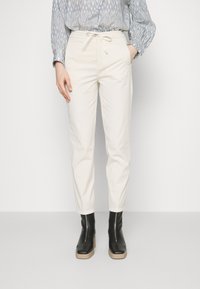 Ljust beiga byxor med dragsko i midjan, insvängda ben och sidofickor, tillsammans med svarta ankelboots med en texturerad sula.