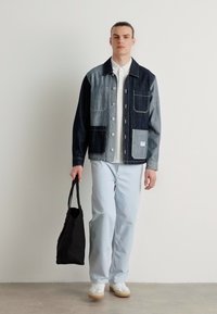 Jeansjakke med to-toners farger, trykknapper og lomme med klaff. Båret over en hvit skjorte med lyseblå bukser og en svart totebag.