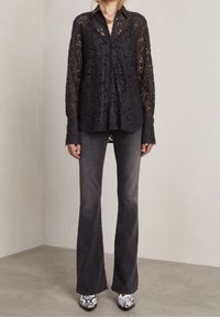 Camicia nera in pizzo con abbottonatura frontale, maniche lunghe e motivo floreale, abbinata a jeans scuri a zampa d'elefante e stivaletti con tacco stampati.