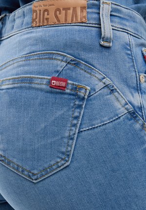 Stražnji džep svijetlo plavih traperica s crvenom oznakom "BIG STAR" i smeđom kožnom zakrpom ušivenom iznad pojasa.