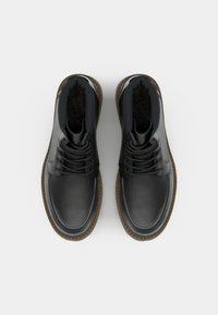 Zapatos de cuero negro con punta redonda y diseño de corte bajo. Presentan cordones oscuros y una suela de goma marrón. Textura suave. Sin logotipos visibles.