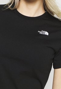 Černé bavlněné tričko s krátkými rukávy, na levé straně hrudi malý bílý nápis „The North Face“. Měkká textura, klasický střih.