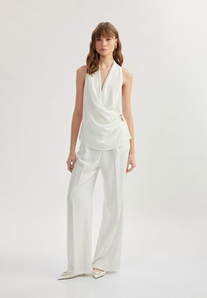 Witte mouwloze top met gedrapeerd ontwerp, voorzien van een gouden accent bij de taille, gecombineerd met wijde broek in bijpassende kleur.