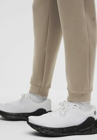 Hvide sportssko med åndbart mesh-overdel og sort splittet sål. Kombineret med beige sweatpants med opkrøllede kanter.