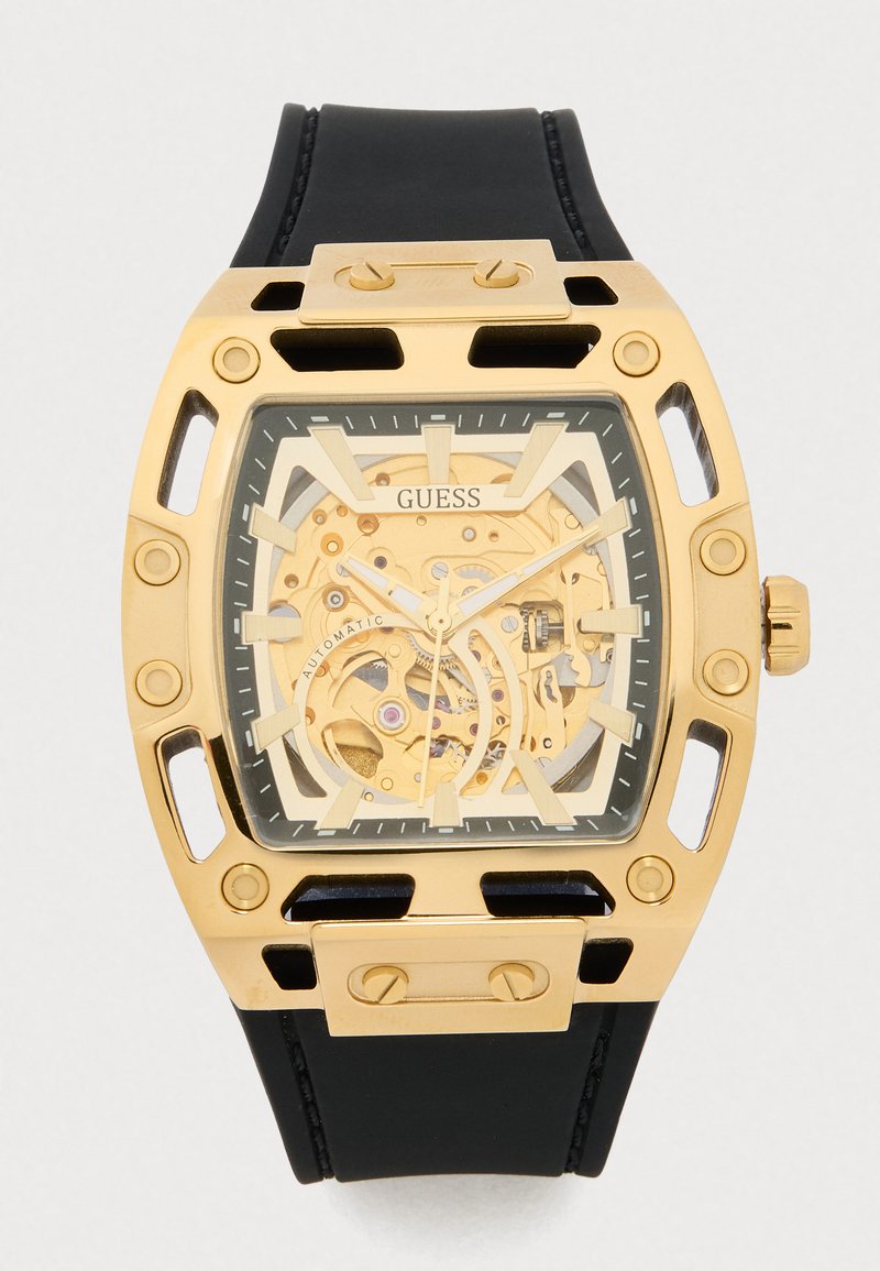 Relógio automático em tom dourado com mostrador quadrado, design esqueleto, bracelete de silicone preto e grandes acentos metálicos que exibem os intricados mecanismos interiores.