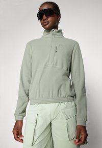 Light green fleece pullover with a half-zip collar, ribbed cuffs, and a zippered chest pocket, paired with light green cargo pants.